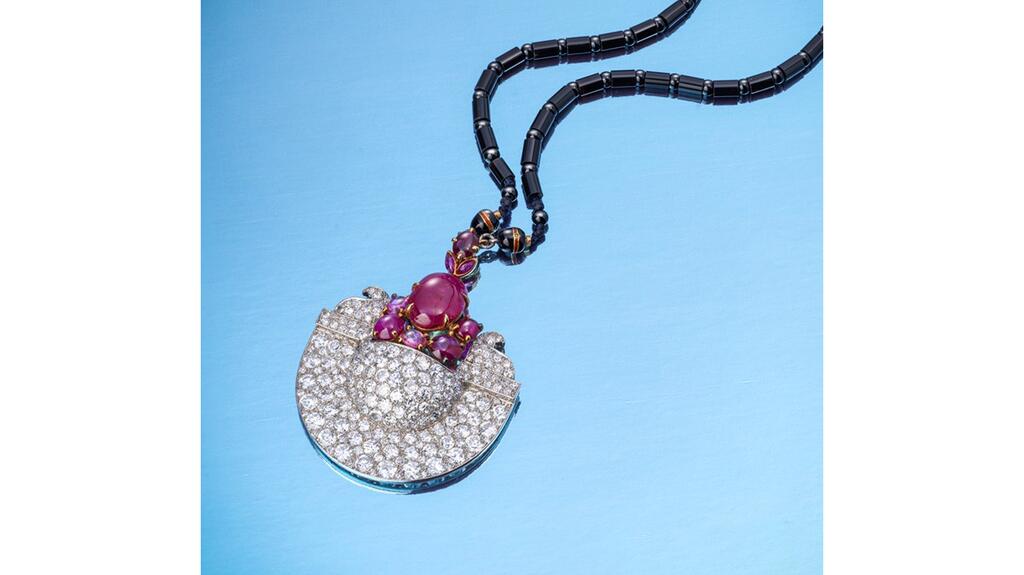 The Cartier necklace features a pendant pavé set with circular-cut diamonds holding an abstract floral arrangement of cabochon rubies mounted in platinum and gold. It hangs from a chain of black onyx beads. Cartier Art Deco Egyptian necklace